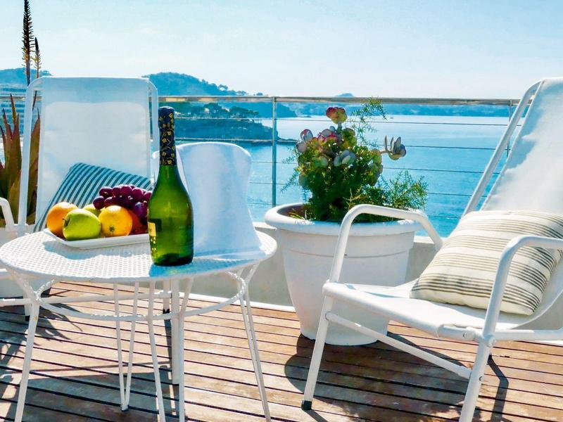 Dvě bílé lehátka na dřevěné terase s ovocem a vínem s výhledem na moře.