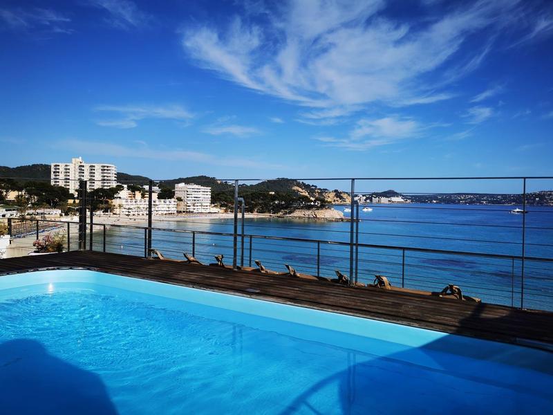 Výhled na bazén s modrou vodou a mořským zálivem v pozadí pod modrou oblohou.