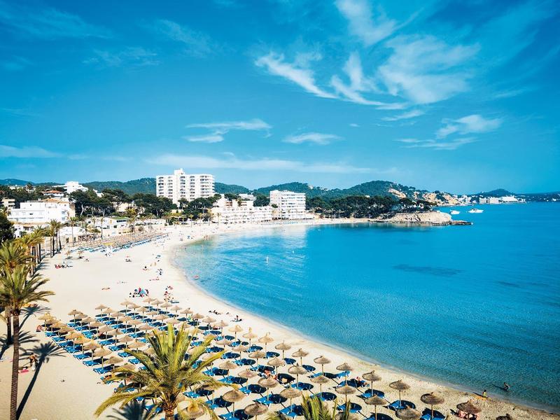 Pláž s slunečníky, palmami a hotely pod modrou oblohou u moře.