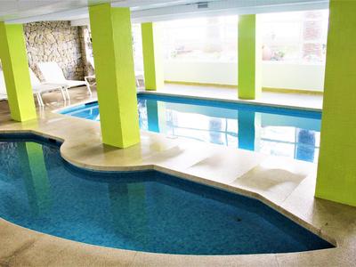 Wnętrze z dwoma basenami, jasnymi filarami i leżakami w tle.