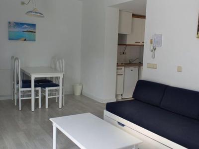 Salon z niebieską sofą, białym stolikiem kawowym i małym stołem jadalnym z czterema krzesłami.