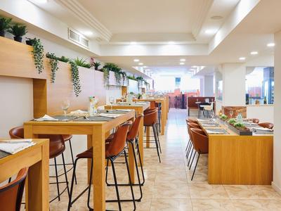 Helles, modernes Restaurant mit Holz- und Ledermöbeln, grünem Pflanzen-Dekor und klarer Raumaufteilung.