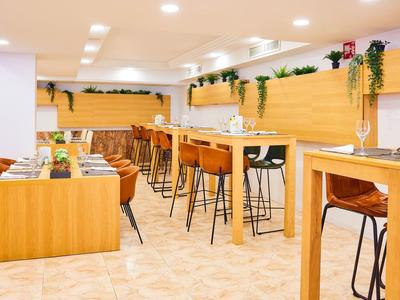 Nowoczesny bar hotelowy z drewnianymi stołami, stołkami barowymi i zielonymi roślinami na ścianie.