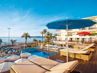 Poolbereich mit Liegen und Sonnenschirmen am Meer bei klarem Himmel und Palmen.