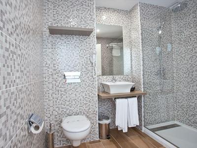 Nowoczesna łazienka z mozaikowymi płytkami, podwieszanym WC, umywalką i kabiną prysznicową.