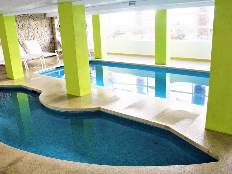 Wnętrze z dwoma basenami, jasnymi filarami i leżakami w tle.