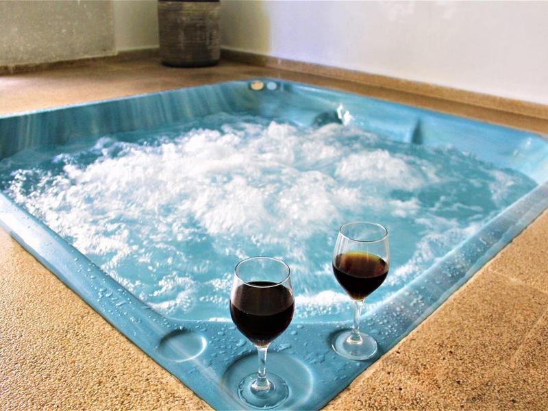 Niebieski jacuzzi z burzliwą wodą i dwoma kieliszkami czerwonego wina na krawędzi.