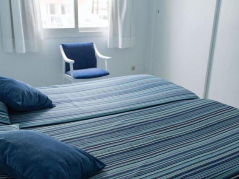 Jasna sypialnia z łóżkami i niebieskimi poduszkami obok okna z zasłonami.