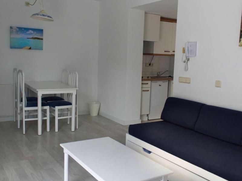 Salon z niebieską sofą, białym stolikiem kawowym i małym stołem jadalnym z czterema krzesłami.