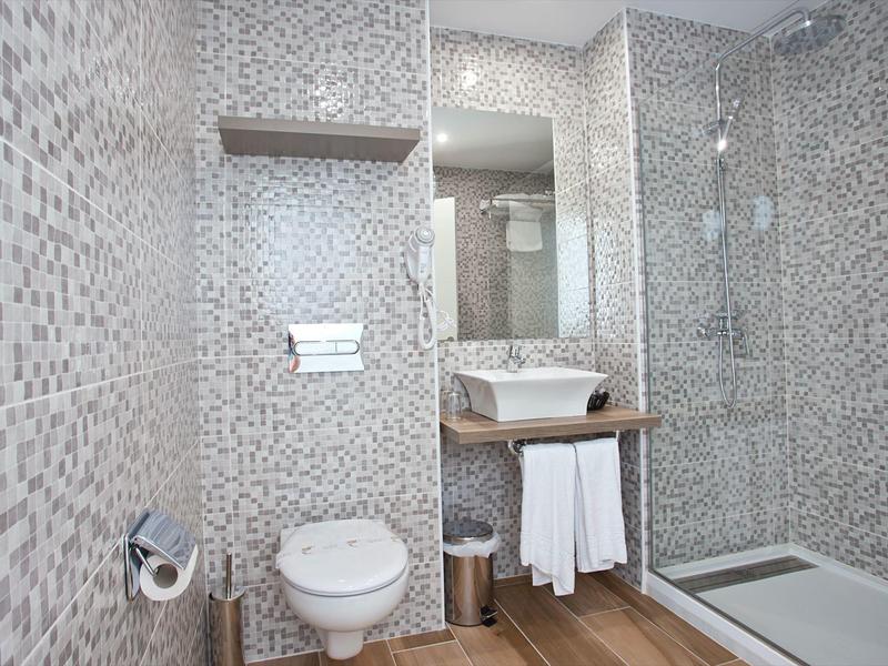 Nowoczesna łazienka z mozaikowymi płytkami, podwieszanym WC, umywalką i kabiną prysznicową.