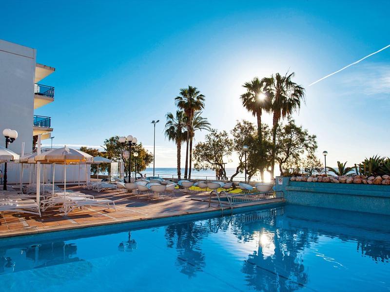 Basen hotelowy z leżakami i palmami o zachodzie słońca nad morzem