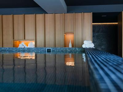 Innen-Pool mit Holzpaneelen, warmem Licht und reflektierender Wasseroberfläche in ruhiger Atmosphäre.