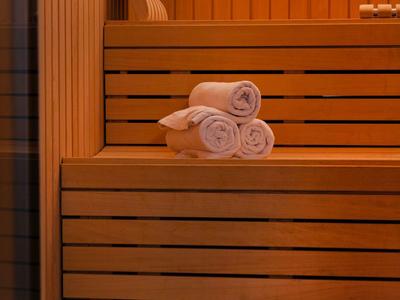 Sauna mit Holzbank, drei weißen Handtüchern und Holzwandverkleidung in warmem Licht.