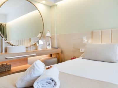 Modern hotel room with round mirror, single bed, and towels on the bed.