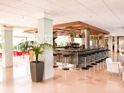 Modern eingerichtete Bar mit Hockern, weißen Wänden, großen Fenstern und hellen Fliesenboden.