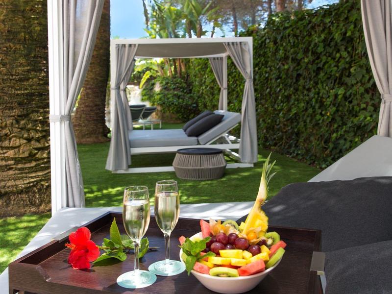 Tropical fruits and drinks on a table beside a lounge and a gazebo in the garden.