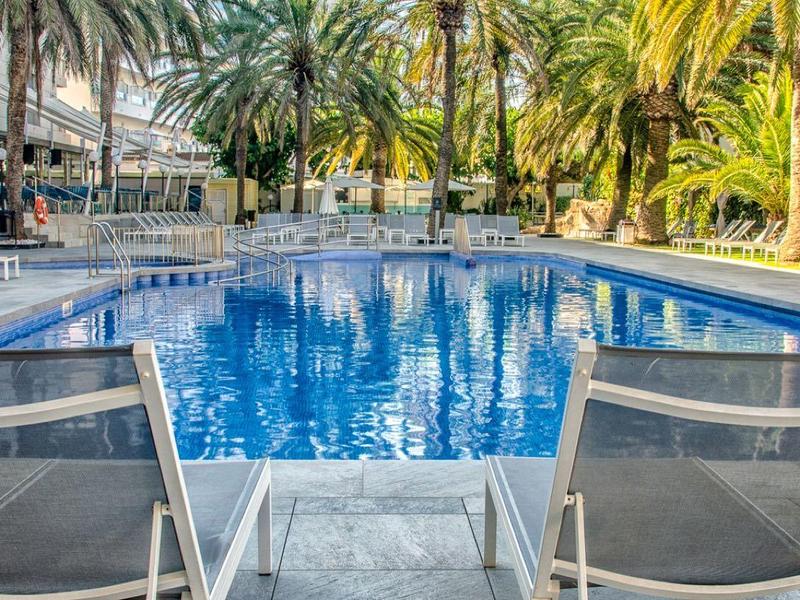 Pool area with blue lounge chairs and palm trees in the background at a hotel.