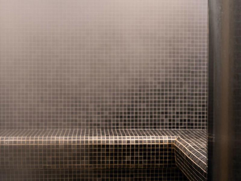 Steamy indoor pool with dark mosaic tiles and metal handrail.