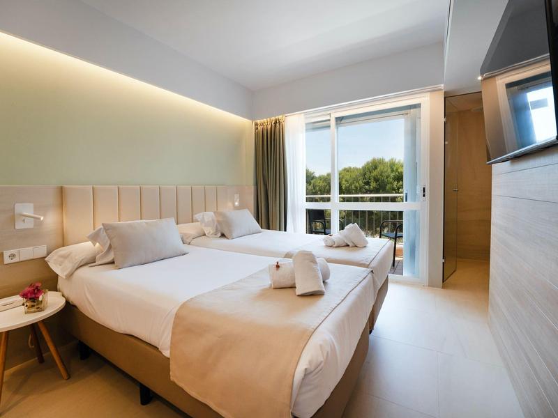 Modern hotel room with two single beds, balcony, and view of trees.