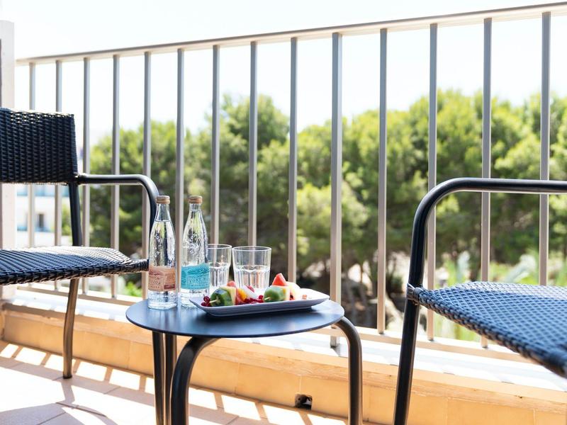 Balcony with two chairs and a table with drinks and snacks, view of green trees.