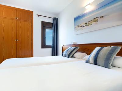 Helles Schlafzimmer mit zwei Einzelbetten, Holzmöbeln, Fenster und maritimem Wandbild.