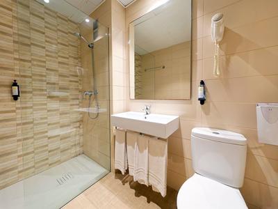 Modernes Badezimmer mit beiger Fliesenwand, Dusche, Waschtisch, Spiegel und WC.