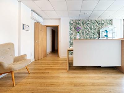 Heller Empfangsbereich mit Holzboden, grauem Sessel, weißen Wänden und farbiger Wanddekoration.