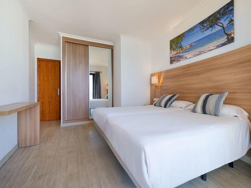 Hell eingerichtetes Schlafzimmer mit großem Bett, Holzverkleidung, Schrank und Strandbild an der Wand.