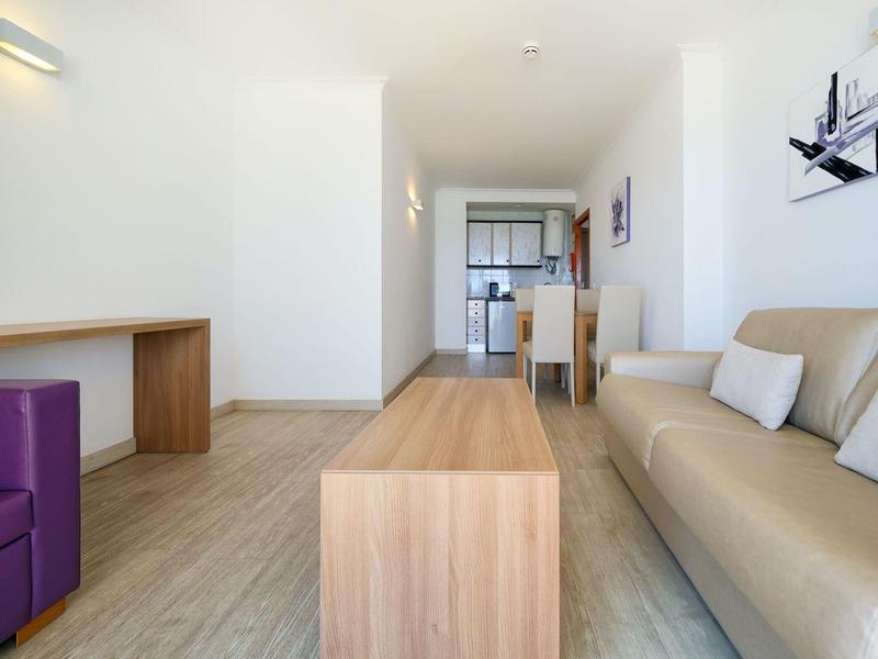 Heller Wohnraum mit beigem Sofa, lila Sessel, Holztisch und Holzfußboden, minimalistischer Stil.