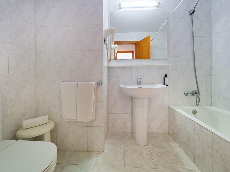 Helles Badezimmer mit weißer Badewanne, Waschbecken, Toilette und Handtuchhalter an der Wand.