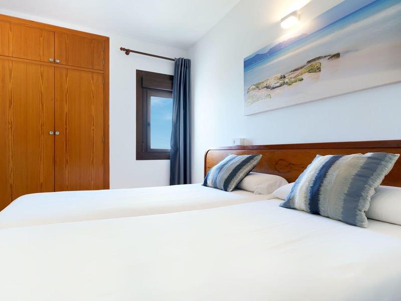 Helles Schlafzimmer mit zwei Einzelbetten, Holzmöbeln, Fenster und maritimem Wandbild.