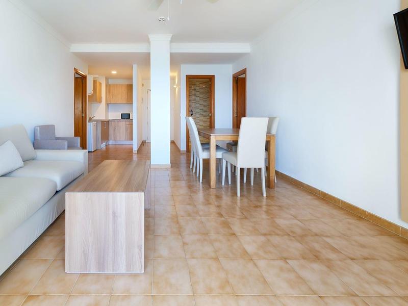 Moderner Wohnraum mit hellen Wänden, grauem Sofa, Holztischen, Essbereich und Fliesenboden.