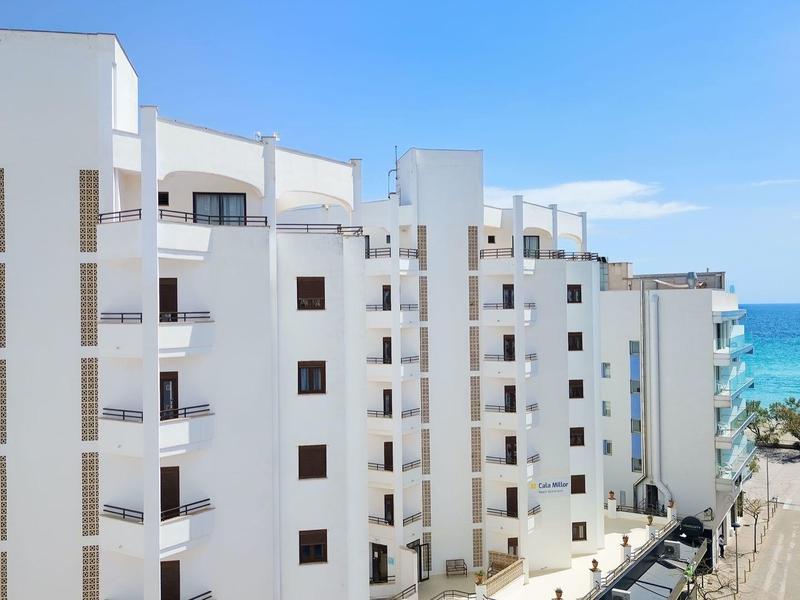 Weiße mehrstöckige Wohngebäude mit Balkonen nahe blauer Küste und Strand unter klarem Himmel.