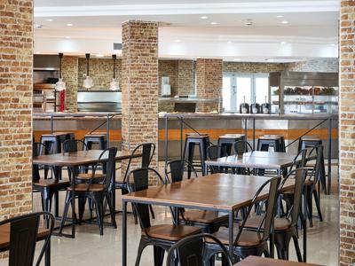 Nowoczesna restauracja hotelowa z drewnianymi stołami, czarnymi krzesłami i ceglaną ścianą.