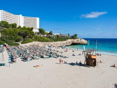 Szeroka piaszczysta plaża z parasolami i hotelem na zielonym wzgórzu pod niebieskim niebem.