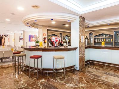 Jasna lobby hotelowa z barem, stołkami barowymi i marmurową podłogą.