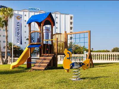 Kolorowy plac zabaw dla dzieci ze zjeżdżalnią na zielonej trawie przed budynkiem hotelu.