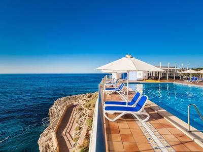 Basen typu infinity z leżakami i parasolem na klifie z widokiem na morze