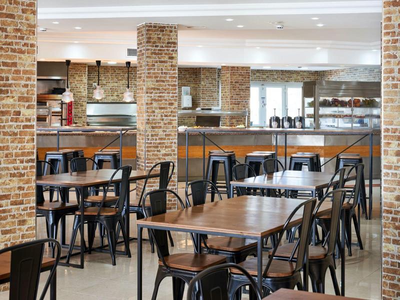 Nowoczesna restauracja hotelowa z drewnianymi stołami, czarnymi krzesłami i ceglaną ścianą.