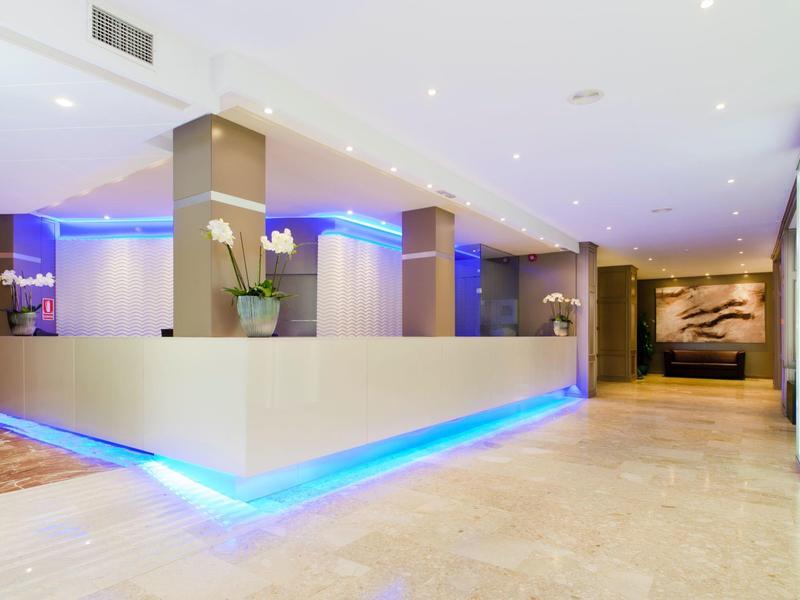 Nowoczesna recepcja hotelowa z oświetlonym kontuarem i jasnymi płytkami podłogowymi.