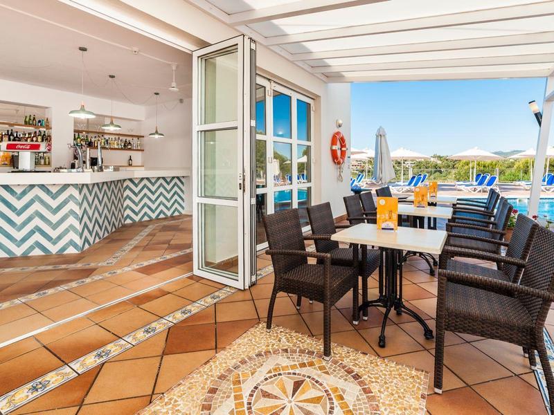 Taras restauracyjny z stołami, krzesłami i widokiem na basen hotelowy.