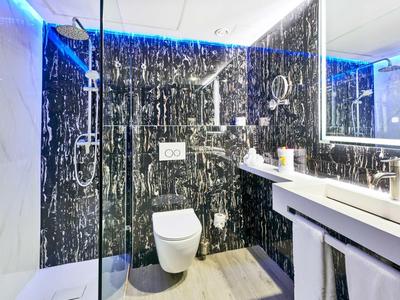 Modernes Badezimmer mit schwarz-weiß gemusterten Wänden, Glasdusche, WC und großem beleuchtetem Spiegel.