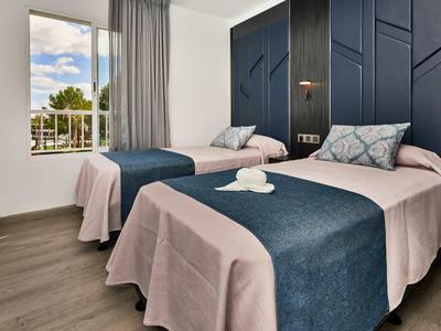 Schlafzimmer mit zwei Einzelbetten, blauen und rosa Bettdecken, großem Fenster und grauen Vorhängen.