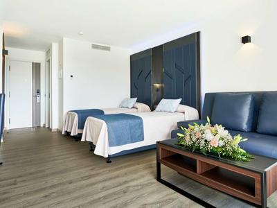 Modernes Hotelzimmer mit Holzboden, blauer Ledercouch, Doppelbett und dunklem Wanddekor.