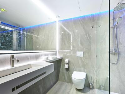 Modernes Bad mit grauen Fliesen, beleuchtetem Spiegel, Waschtisch und Glas-Dusche.