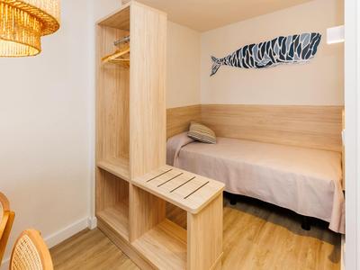 Piccola stanza con letto singolo, armadio aperto e decorazione a forma di pesce sulla parete.