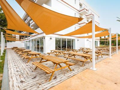 Buitengebied van een hotel met houten picknicktafels en oranje zonneschermen.