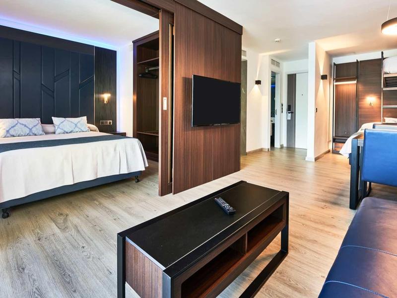 Modern decorated hotel room with blue seating and bathroom in the background.