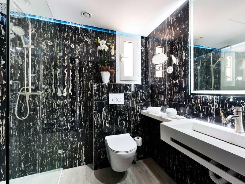 Modern bathroom with black marble walls, walk-in shower, and double sinks.