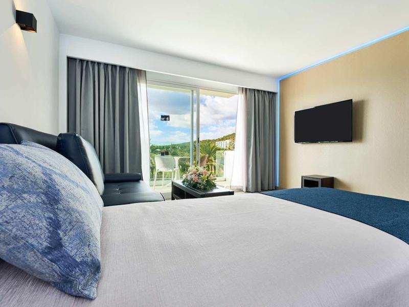 Modern hotel room with large bed, balcony, and view of the landscape.